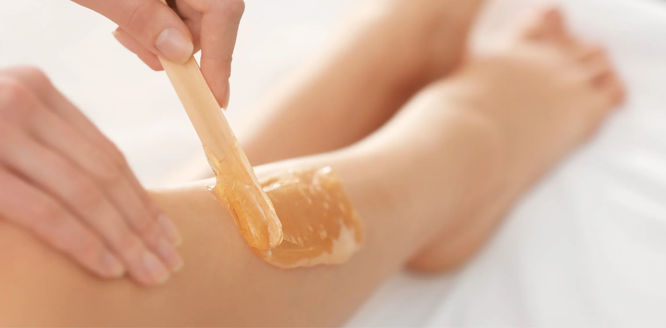 Esthetician applying warm wax during a professional leg waxing service
