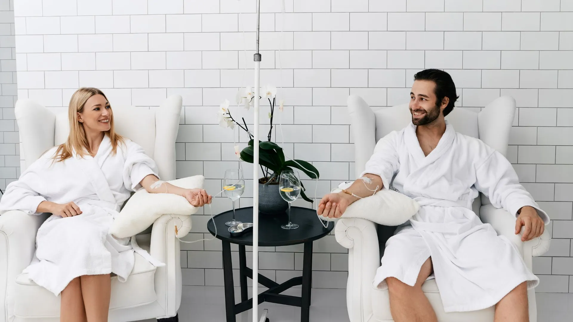 Two clients relaxing side by side during IV drip infusions in a spa suite