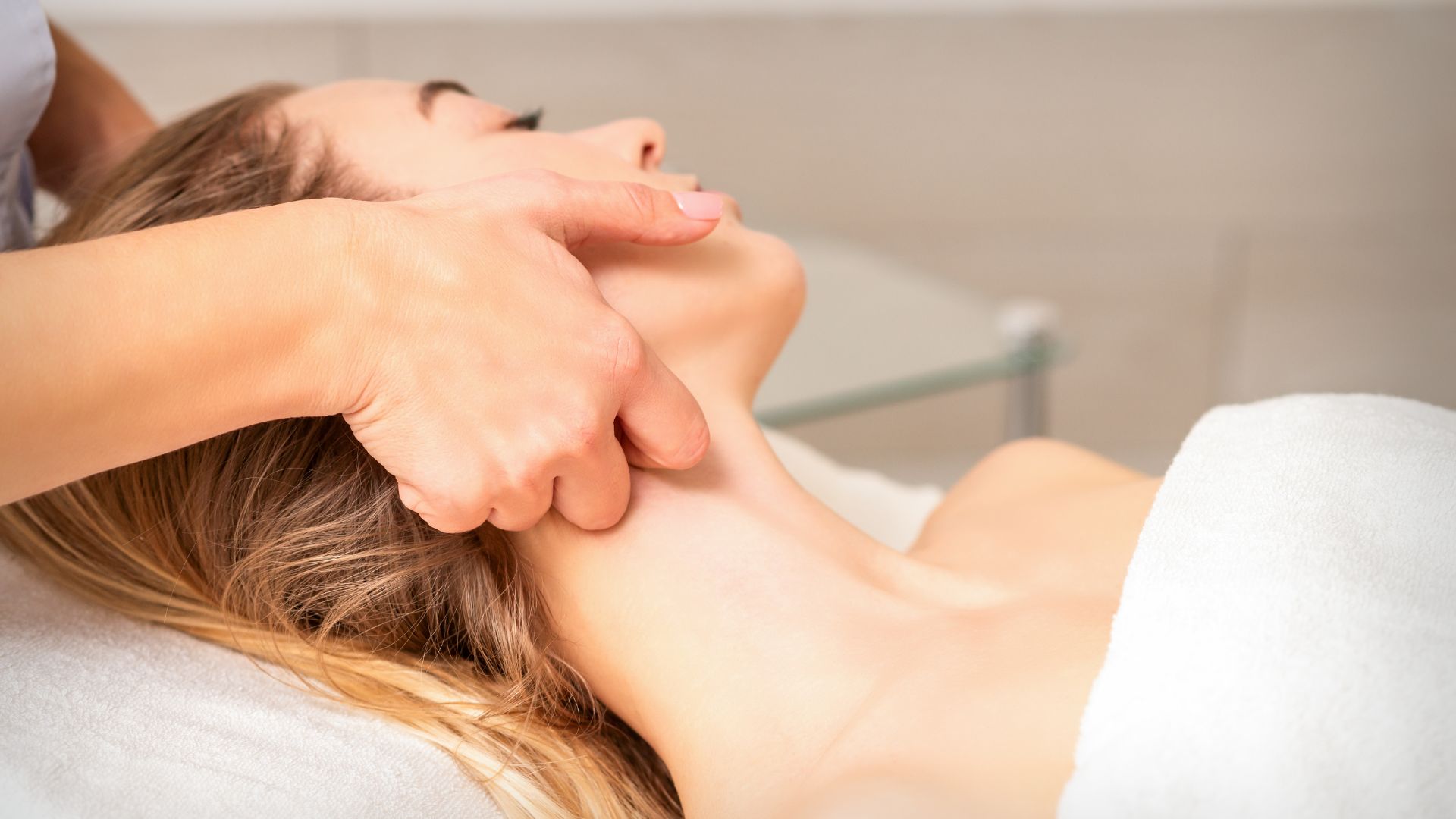 A gentle Manual Lymphatic Drainage massage being performed on the face and neck.